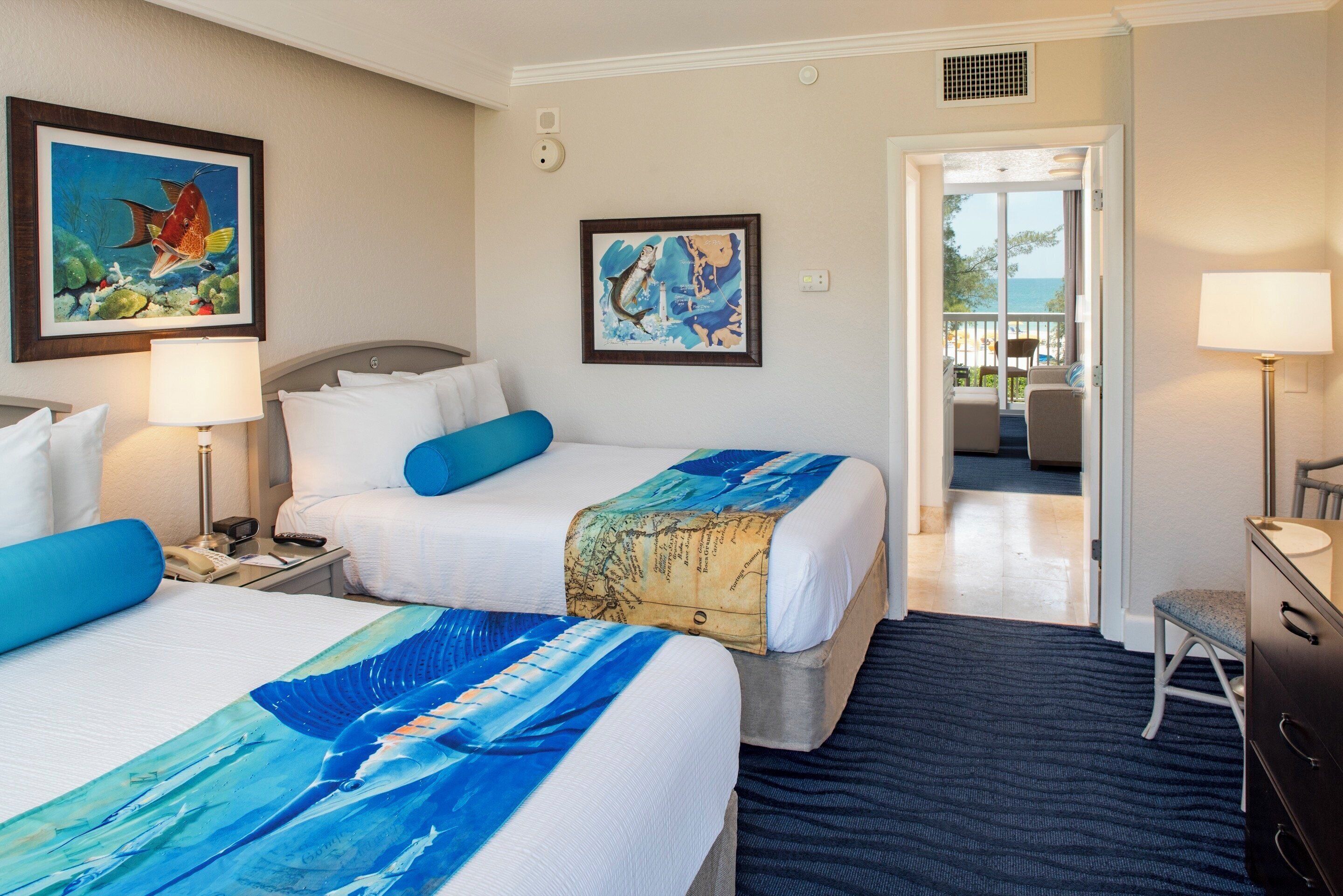 A hotel room with two beds, a desk, a chair, a dresser, and a balcony with a view.