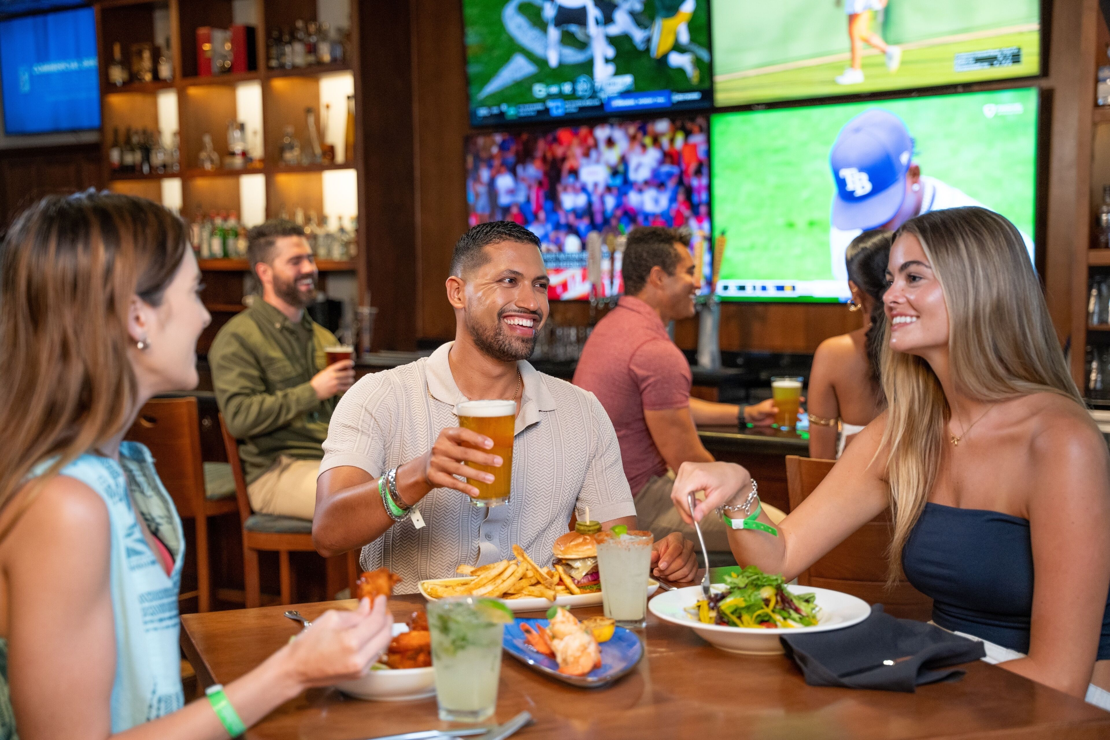 A group of people dining at a restaurant with multiple screens displaying sports events in the background.