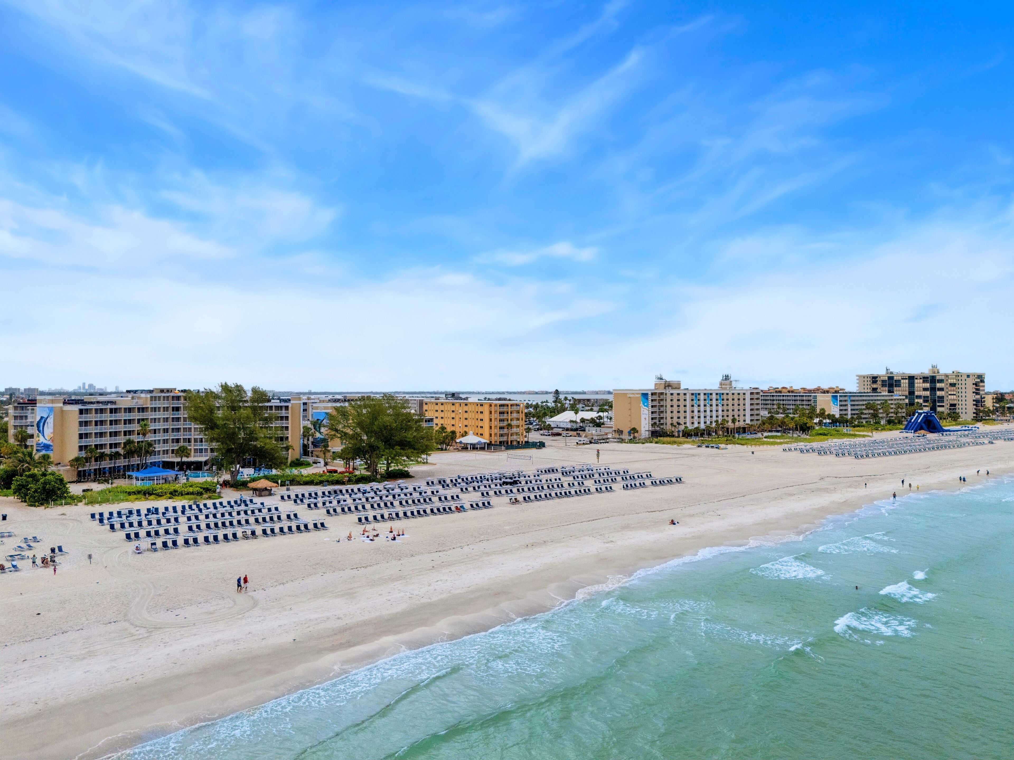 A beach with rows of sun loungers and a hotel in the background.