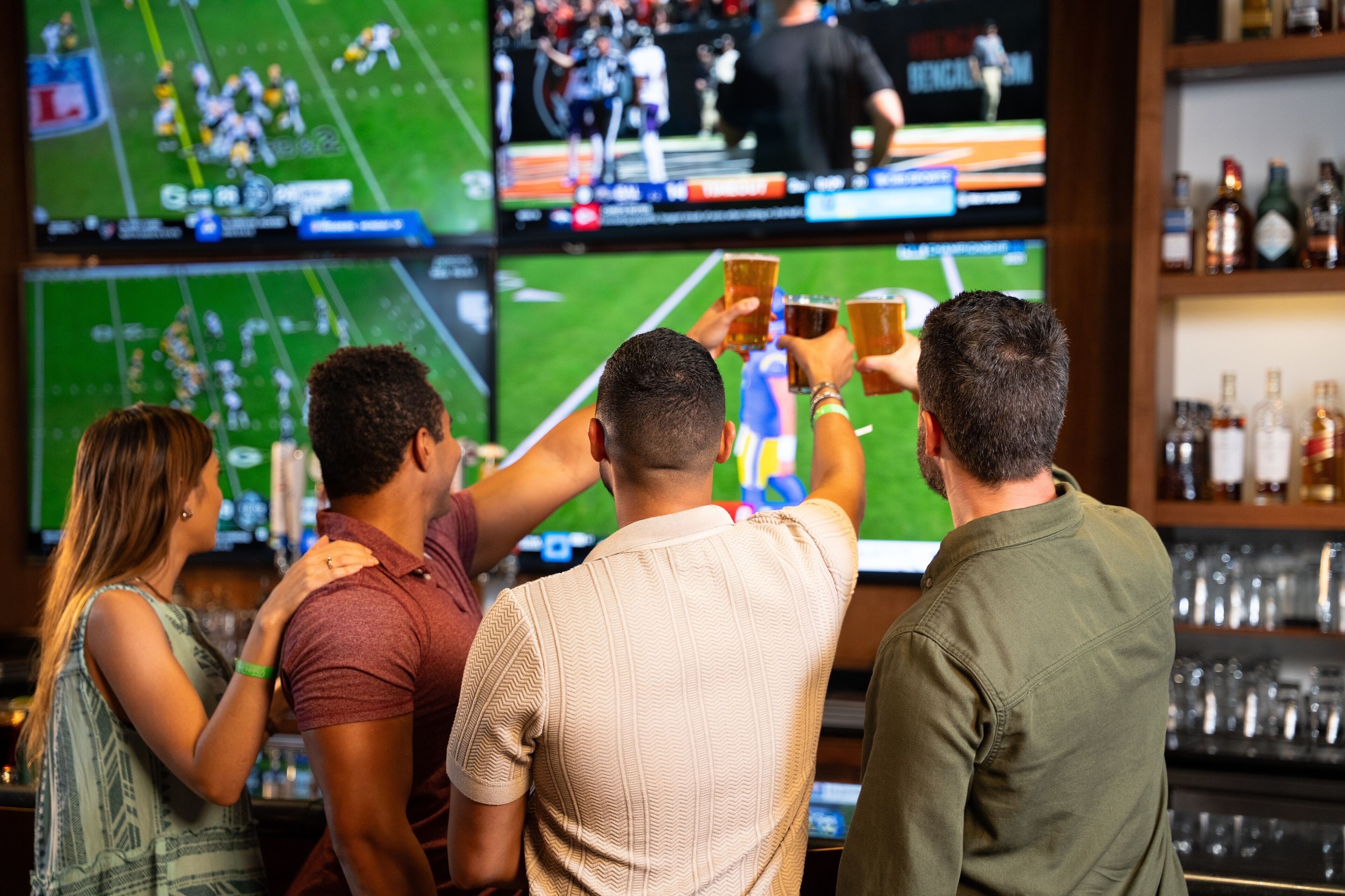 A bar with multiple screens displaying sports games, a bar counter with glasses, and shelves with bottles.