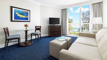 A hotel room with a balcony, a television, a sofa, and a dining area with chairs and a table.