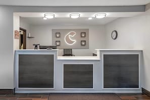 A reception desk with a clock, a wall-mounted sign, and recessed lighting. - Comfort Inn Fergus Falls (Fergus Falls)