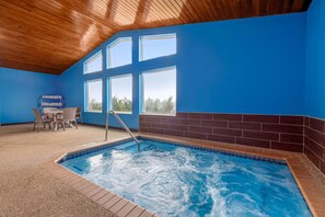 An indoor swimming pool with a wooden ceiling, blue walls, and a seating area with chairs and a table. - Comfort Inn Fergus Falls (Fergus Falls)