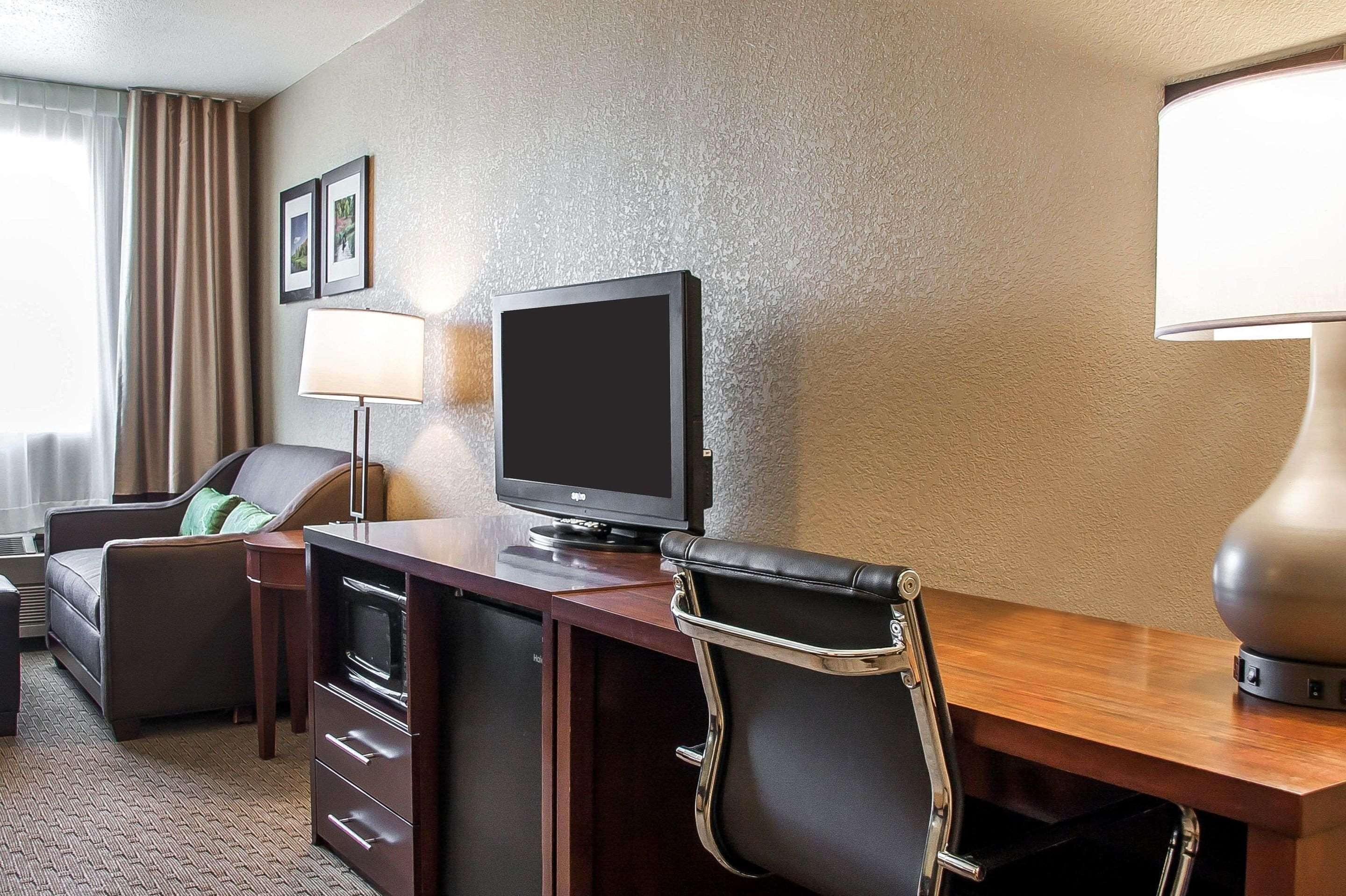 A hotel room with a desk, a television, a lamp, a chair, and a bed.