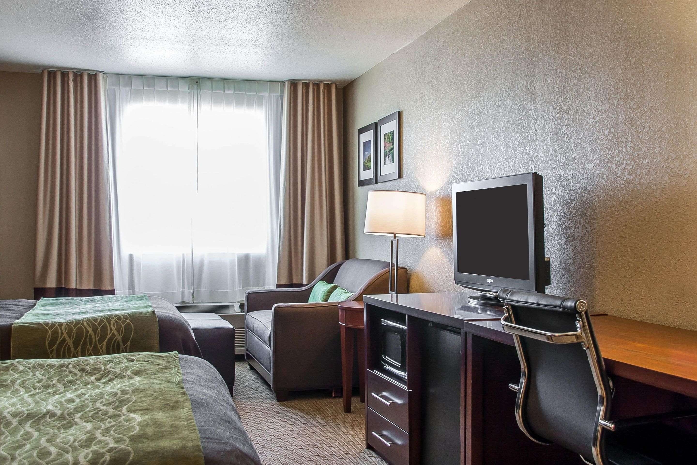 Une chambre d’hôtel avec deux lits, un bureau équipé d’une télévision, une chaise et une lampe.
