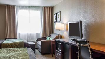 A hotel room with two beds, a desk with a television, a chair, and a lamp.