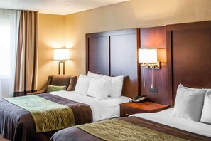 A hotel room with two beds, a wooden headboard, bedside lamps, a telephone, and a window with curtains.