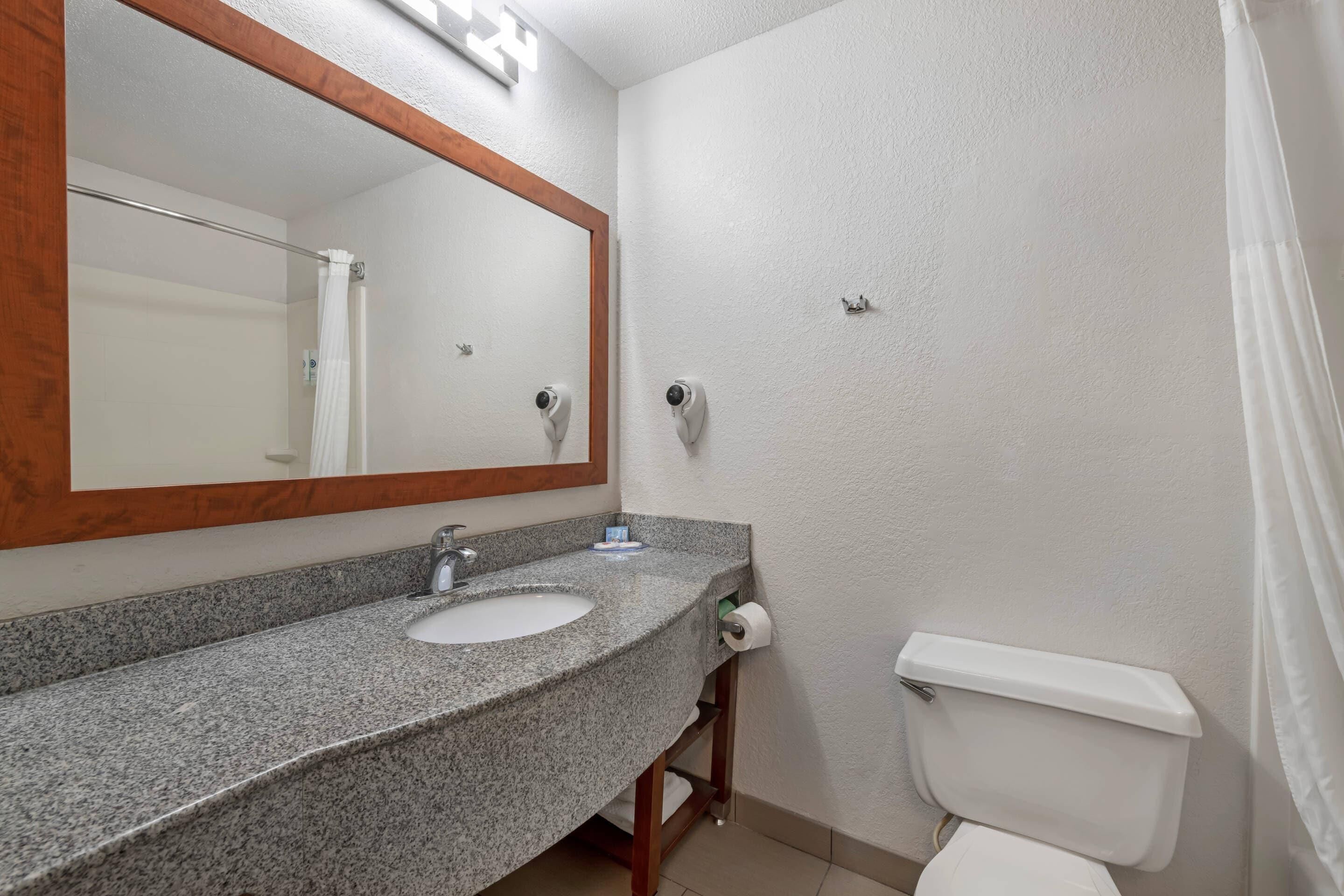 Un baño con lavamanos de granito, un espejo con marco de madera, inodoro y cortina de ducha.