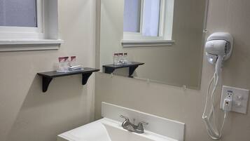 A bathroom with a white sink, a mirror with lights, a hairdryer, and a window.