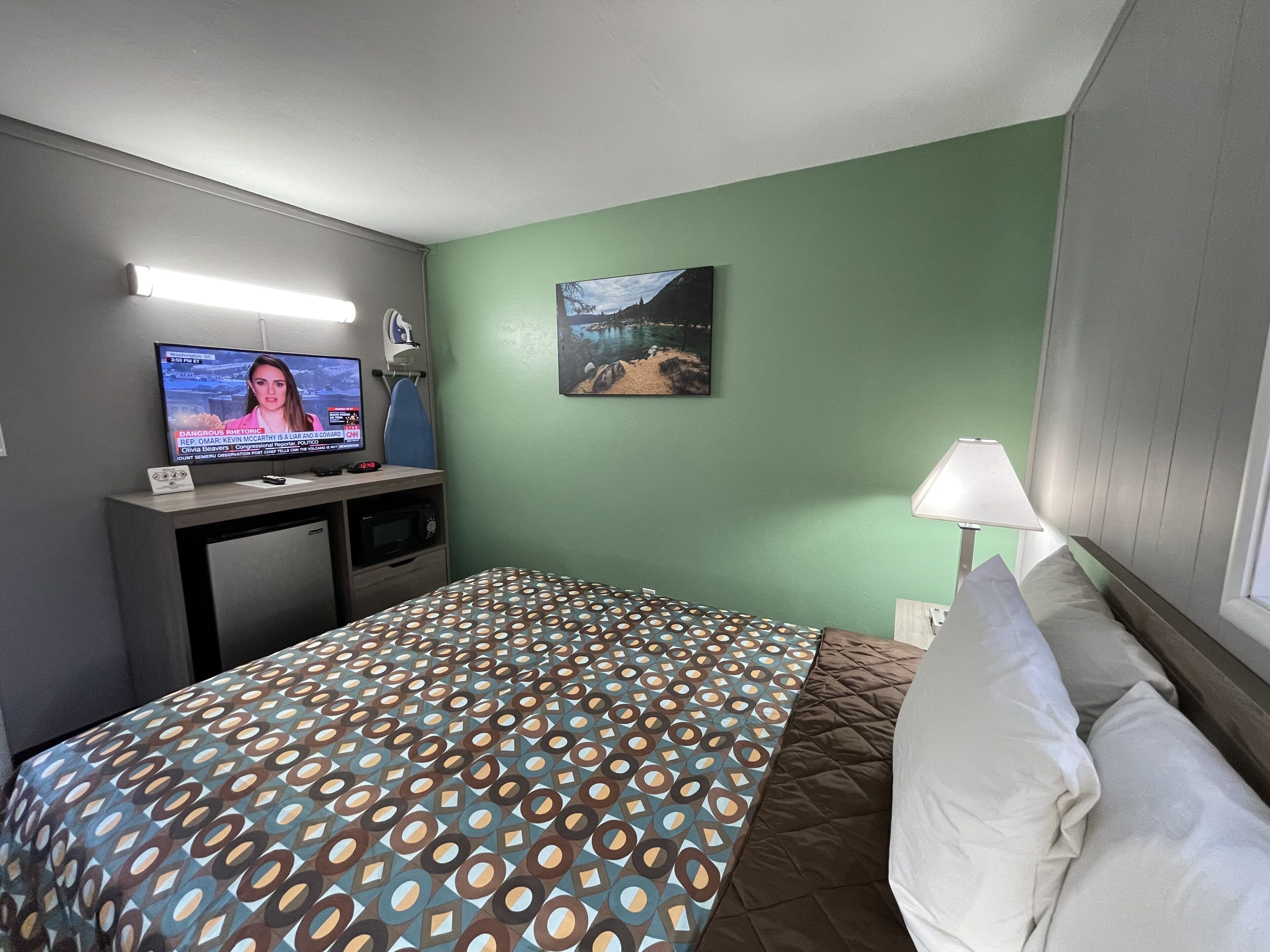Une chambre d’hôtel avec un lit, un bureau avec une télévision, un tableau au mur et une lampe.