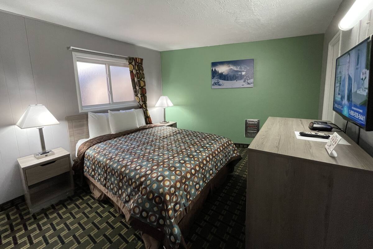 A hotel room with a bed, two bedside tables with lamps, a desk with a computer and a TV, and a window with curtains.