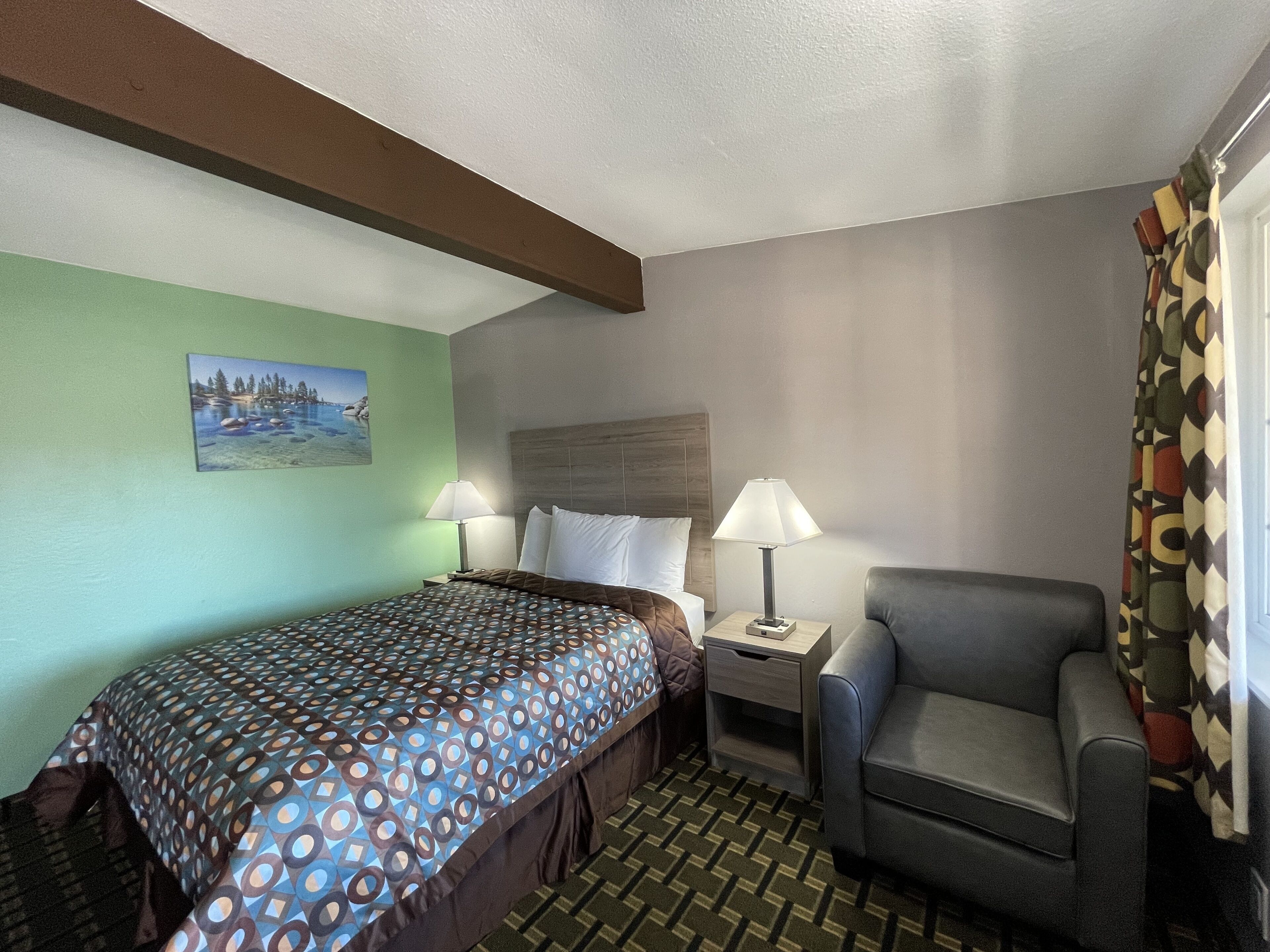 A hotel room with a bed, two bedside tables, a chair, a painting on the wall, and a patterned carpet.
