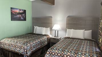 A hotel room with two beds, a nightstand with a lamp, a painting on the wall, and a patterned bedspread.