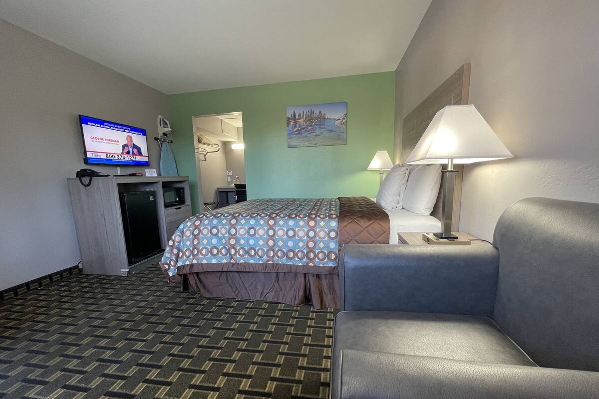 A hotel room with a bed, a desk, a television, a lamp, and a couch.