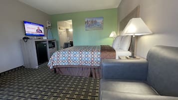 Habitació d'hotel amb llit, escriptori, televisió, làmpada i sofà.