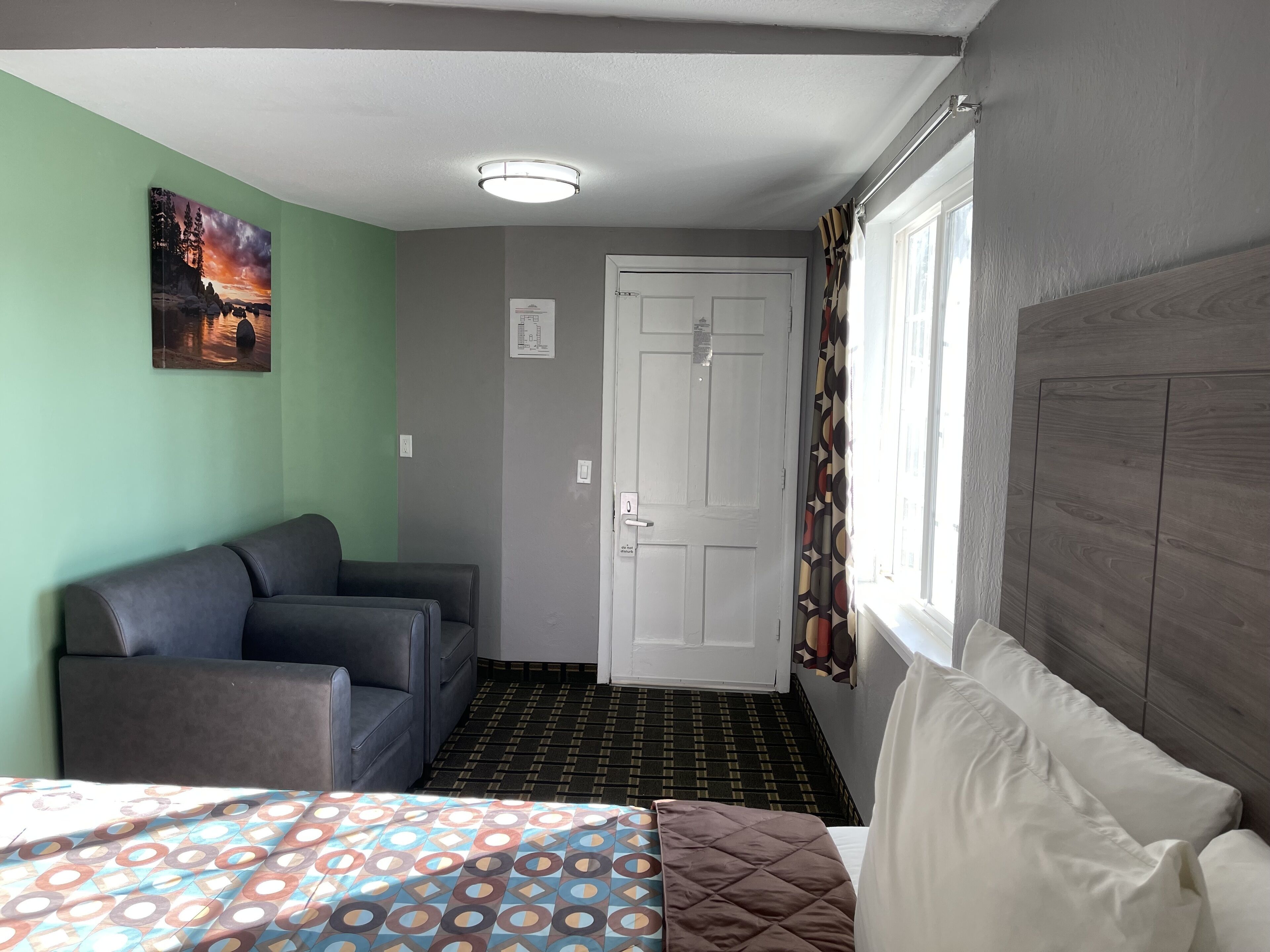 A hotel room with a bed, a sofa, a painting on the wall, and a door.
