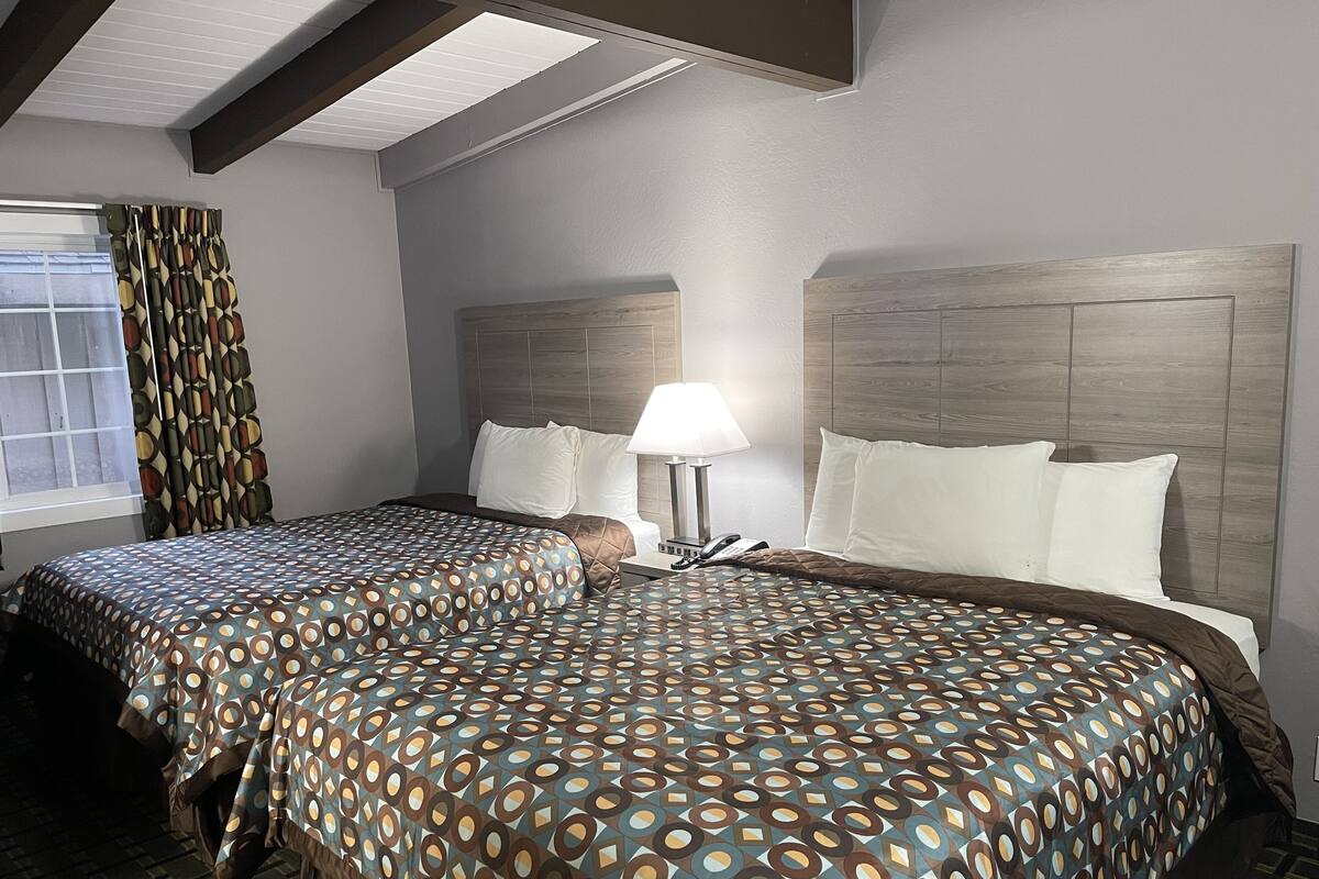 A hotel room with two beds, a window with curtains, a bedside table with a lamp, and a phone.