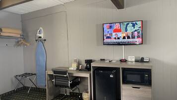 A hotel room with a desk, a television mounted on the wall, a microwave, and a refrigerator.