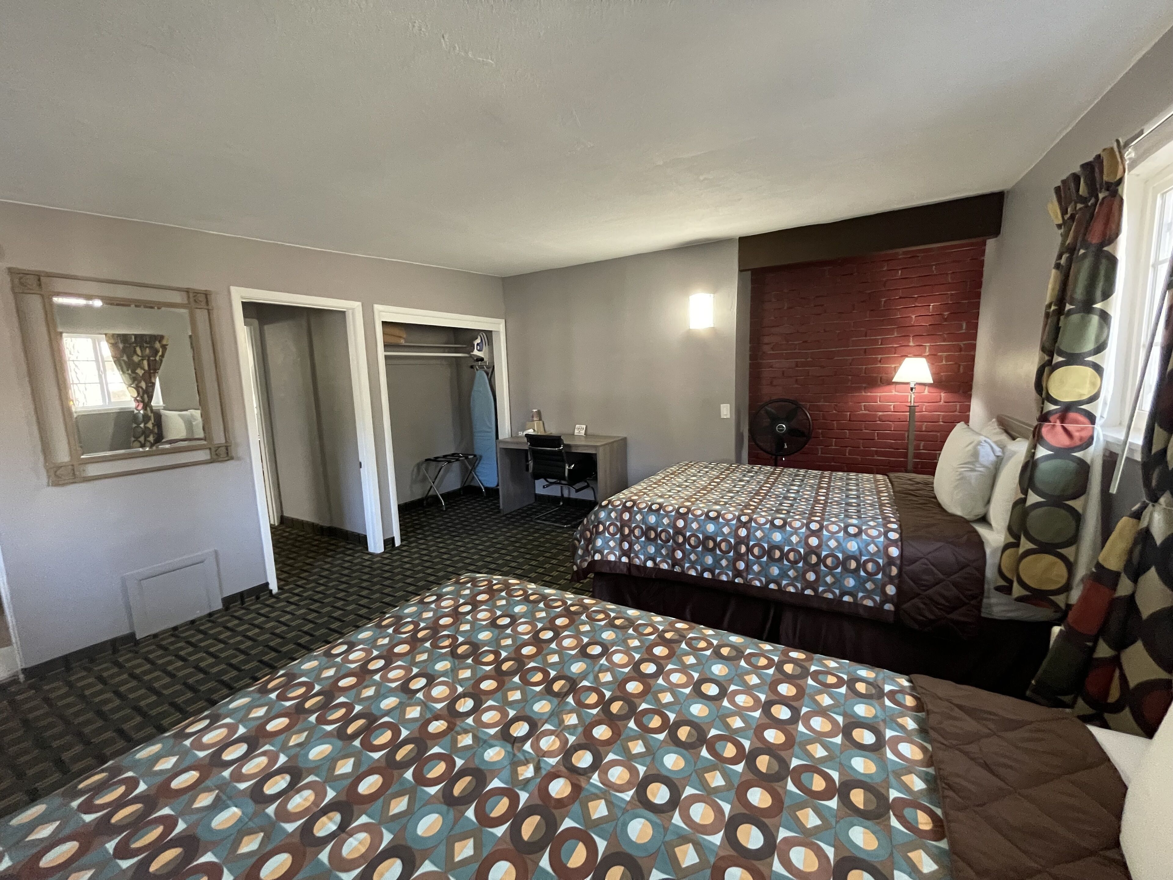 A hotel room with two beds, a desk, a chair, a mirror, and a wardrobe.