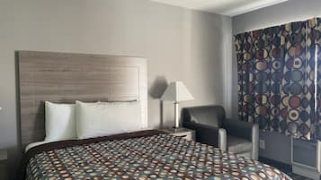 Een hotelkamer met een groot bed, een nachtkastje, een bureau, een stoel en een raam met patroon gordijnen.