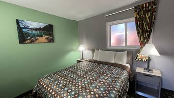 Habitación de hotel con cama, dos mesitas de noche, una ventana con cortinas, un cuadro en la pared y una colcha estampada.