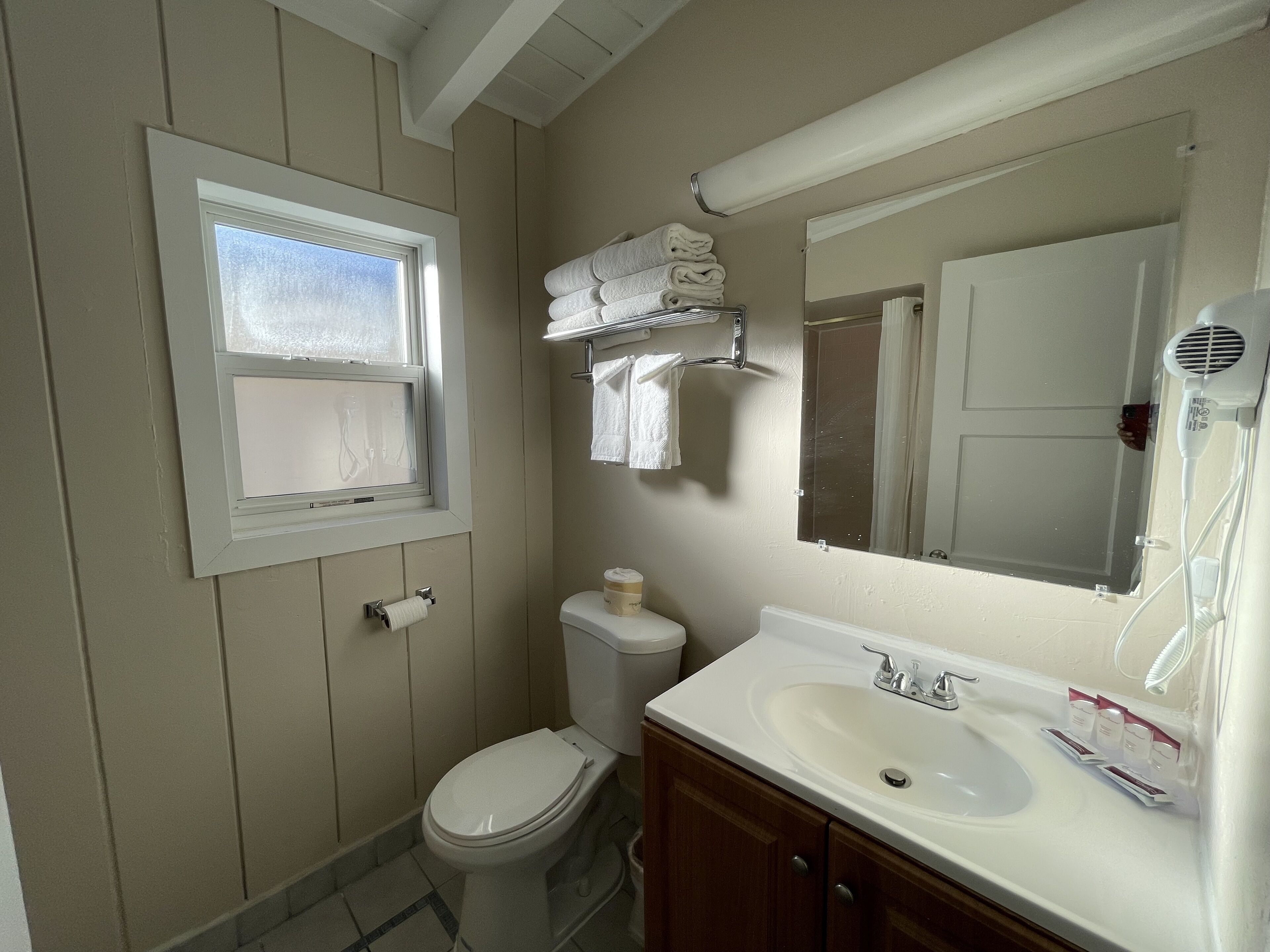Un baño con inodoro, lavamanos, espejo, toallero y ventana.