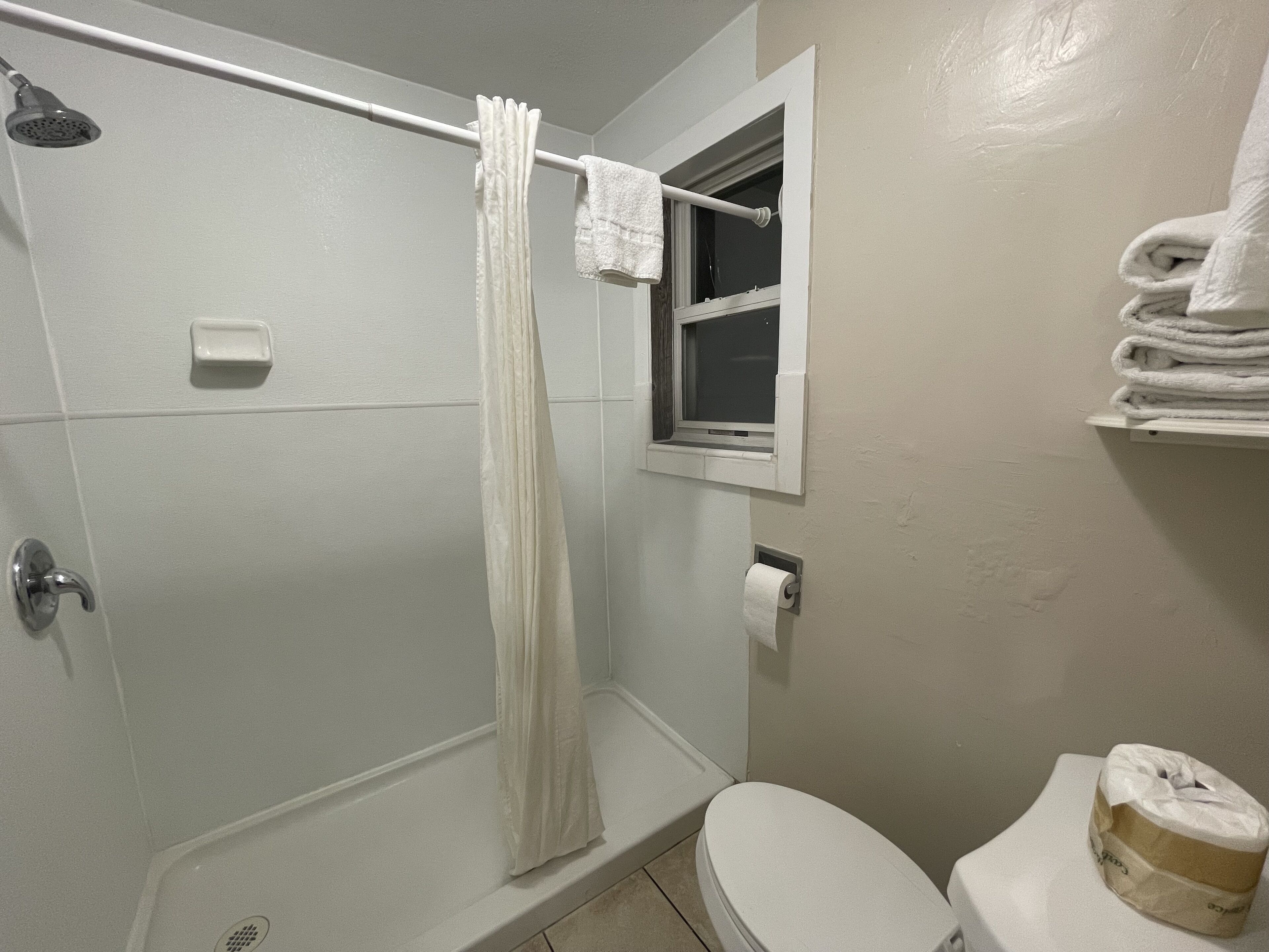 A bathroom with a shower, toilet, and a window.