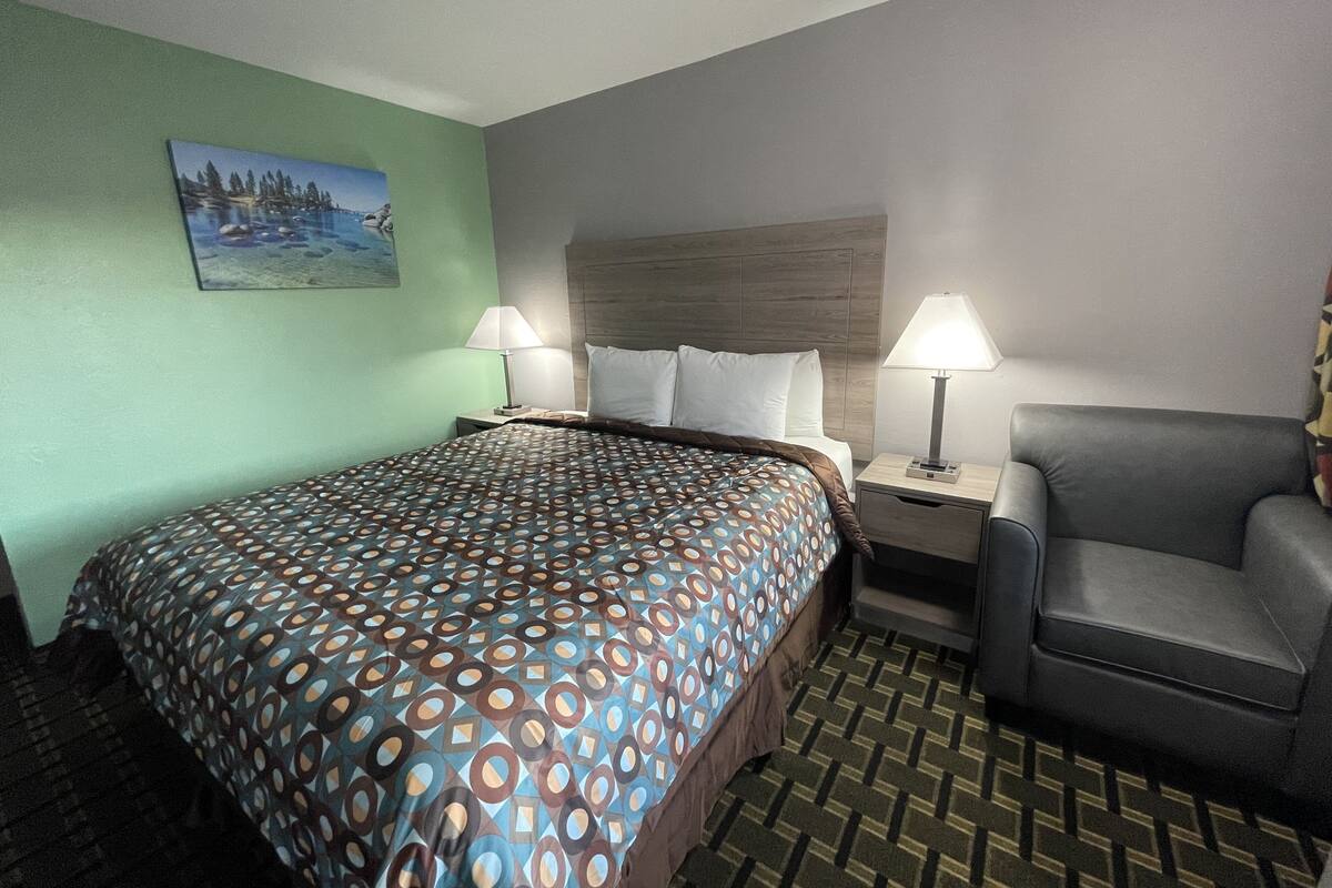 A hotel room with a large bed, two bedside tables with lamps, a chair, and a painting on the wall.