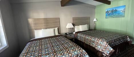 Habitación de hotel con dos camas, una mesita de noche, una lámpara y un cuadro en la pared.