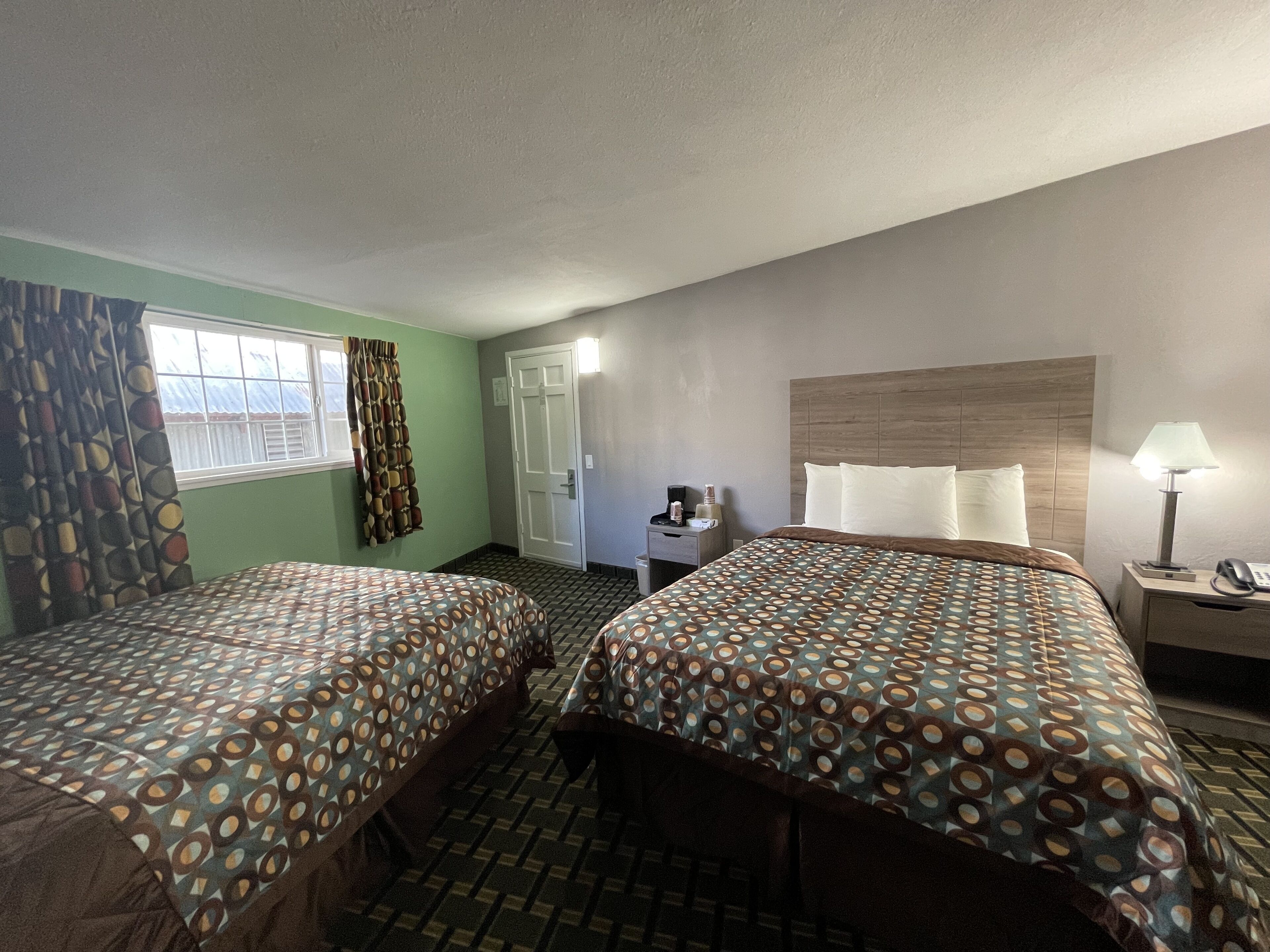 A hotel room with two beds, a desk, a chair, a lamp, and a window with curtains.