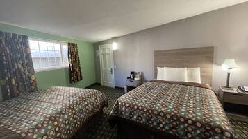 Een hotelkamer met twee bedden, een bureau, een stoel, een lamp en een raam met gordijnen.
