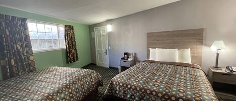 A hotel room with two beds, a desk, a chair, a lamp, and a window with curtains.