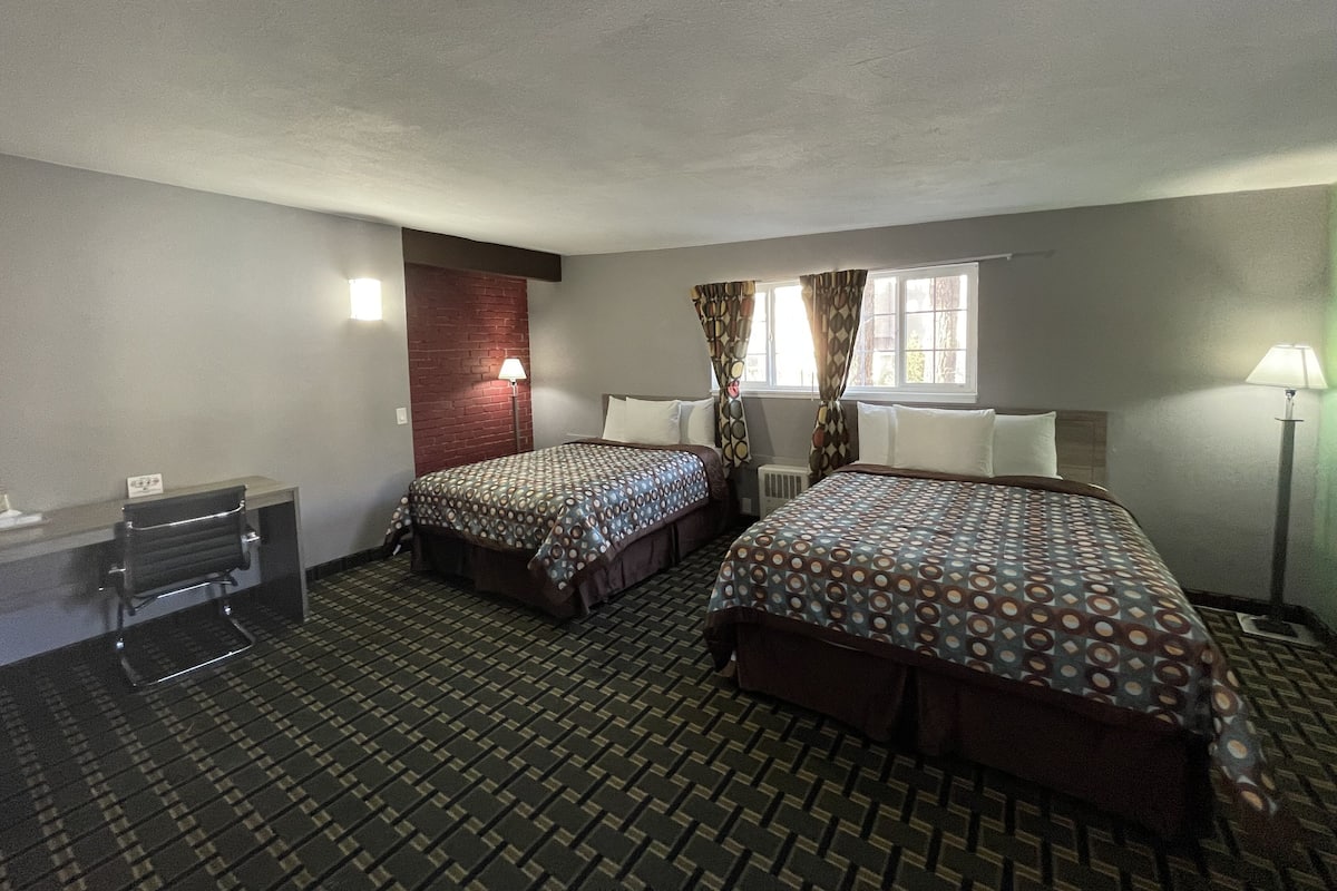 A hotel room with two beds, a desk, and a window.