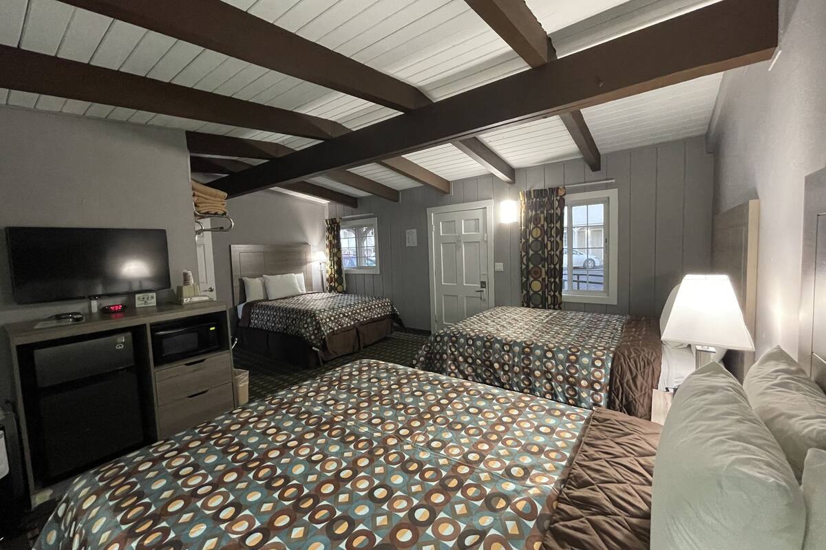 A hotel room with two beds, a TV, a desk, and a window with curtains.
