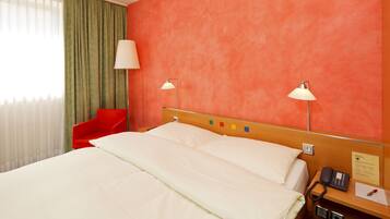 A hotel room with a bed, a red chair, two bedside lamps, a telephone, and a wall-mounted control panel.