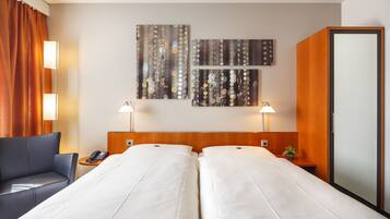 A hotel room with two beds, a sofa, a telephone, wall art, and a mirror.