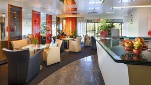 A modern hotel lobby with seating areas, a reception desk, and large windows offering views of the outdoors. - Hotel Metropol Basel (Basel)