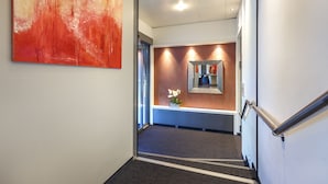 A modern hallway with a red abstract painting, a reception desk, and a staircase. - Hotel Metropol Basel (Basel)