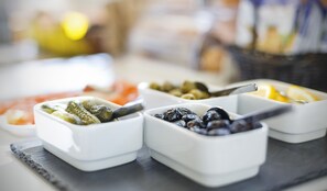 A table with various food items in white bowls, including pickles, olives, and lemons.