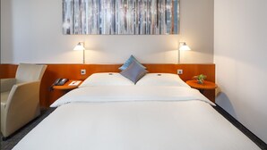 A hotel room with a bed, two bedside tables, a chair, a lamp, and a wall art piece. - Hotel Metropol Basel (Basel)