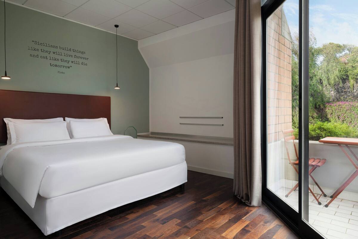 Een moderne slaapkamer met een groot bed, een hoofdbord, een muisquote, een raam en uitzicht op groen buiten.