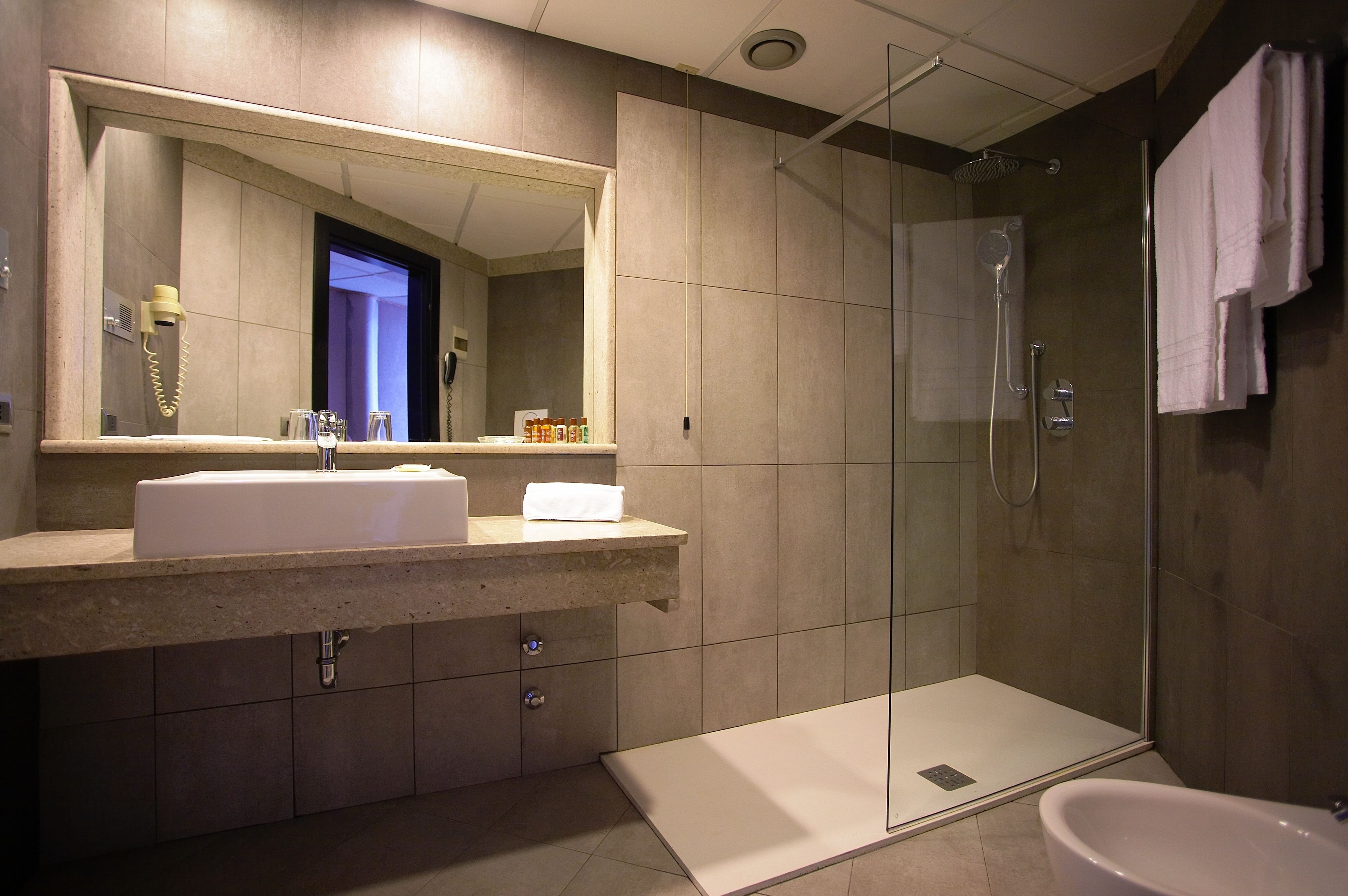 A modern bathroom with a large mirror, a sink, a shower, and a toilet.
