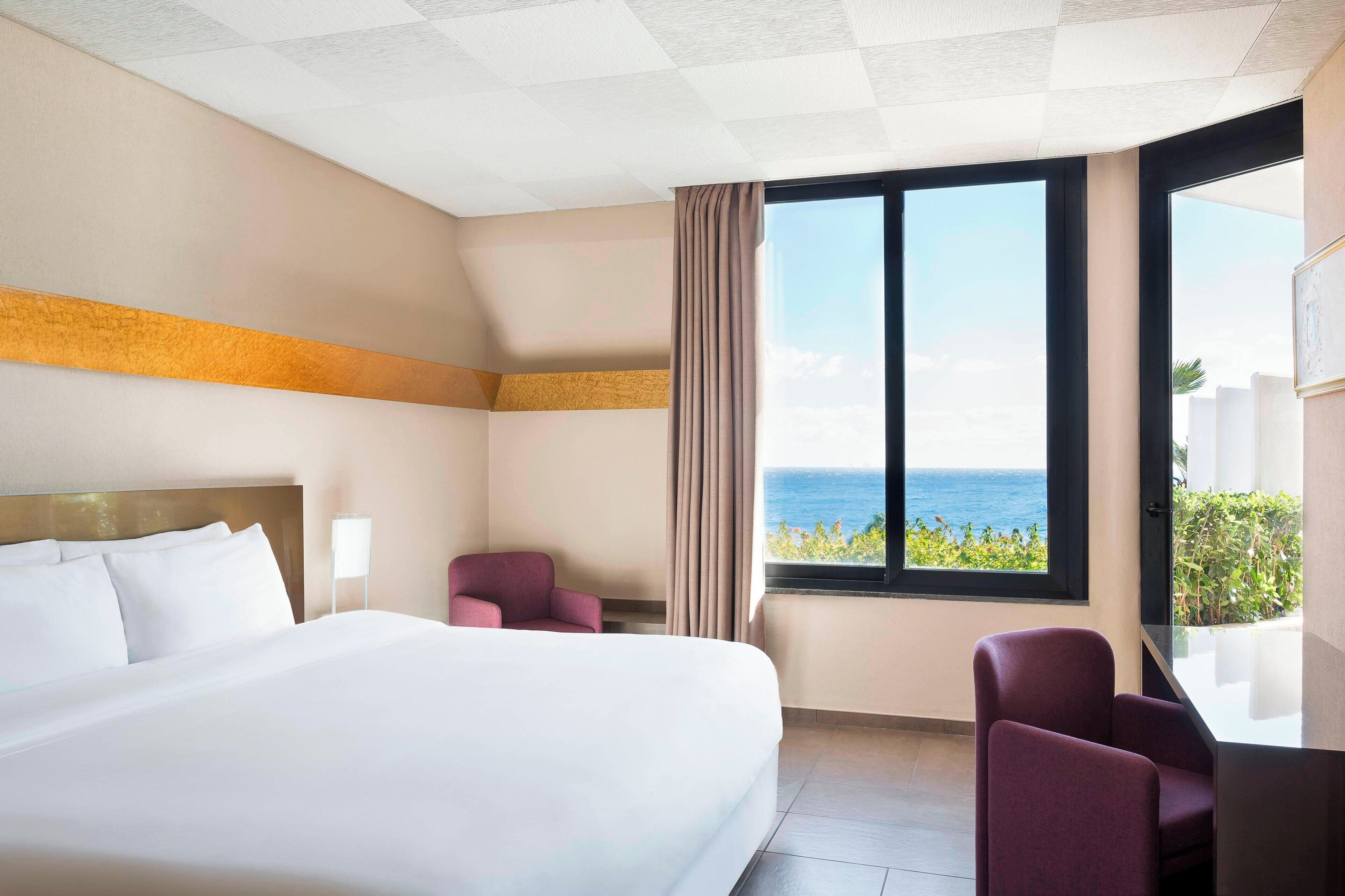 Une chambre d’hôtel avec un grand lit, un bureau, une chaise et une vue sur l’océan.
