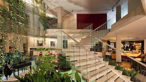 A spacious atrium with a central staircase, surrounded by lush indoor plants and a seating area with a table and chairs. - Four Points by Sheraton Catania Hotel & Conference Center (Aci Castello)