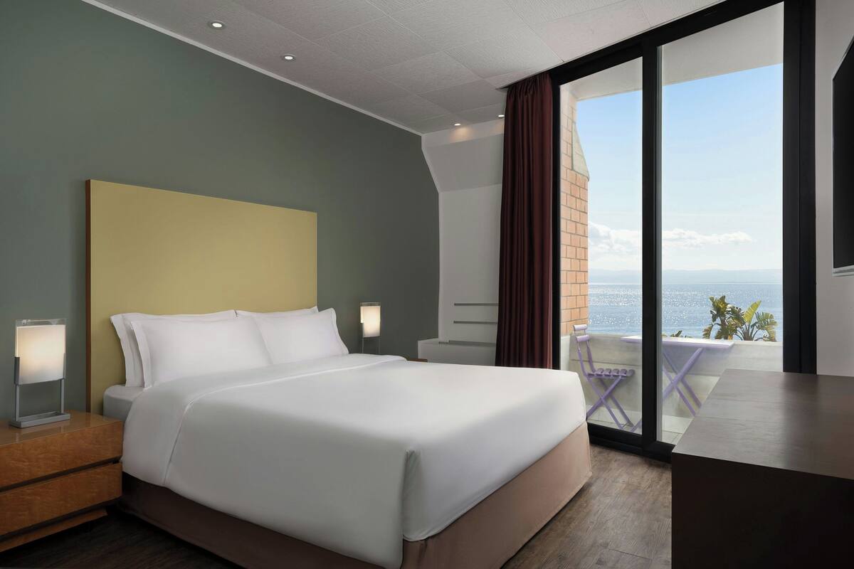 Een moderne hotelkamer met een groot bed, nachtkastje, bureau en uitzicht op zee.