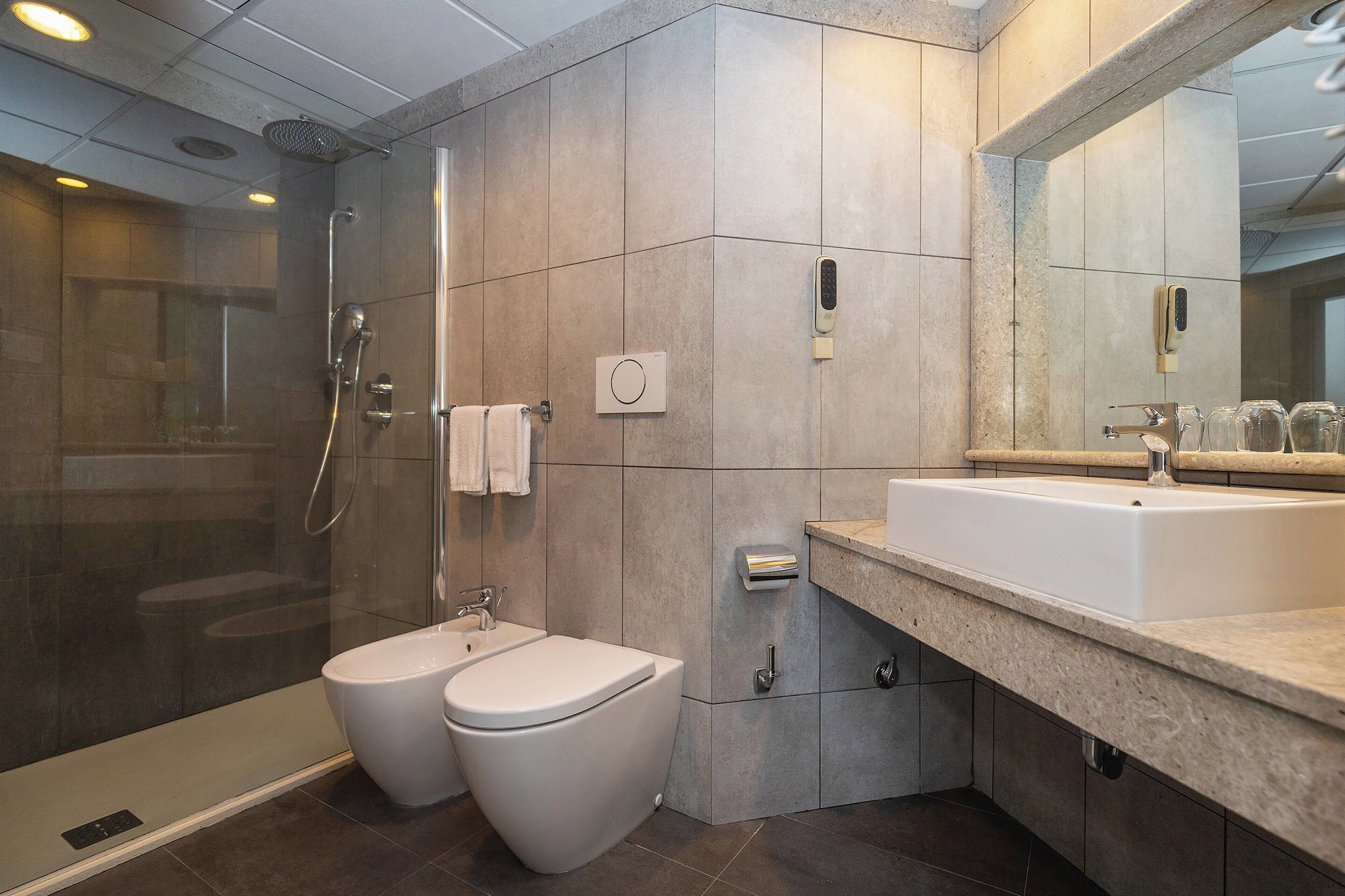 A modern bathroom with a glass-enclosed shower, a standalone toilet, and a large sink with a mirror.