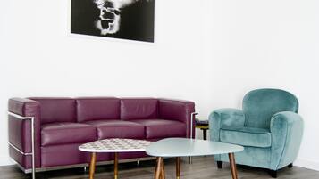 Uma sala de estar moderna com um sofá roxo, uma poltrona verde-água e uma pequena mesa redonda com tampo estampado.