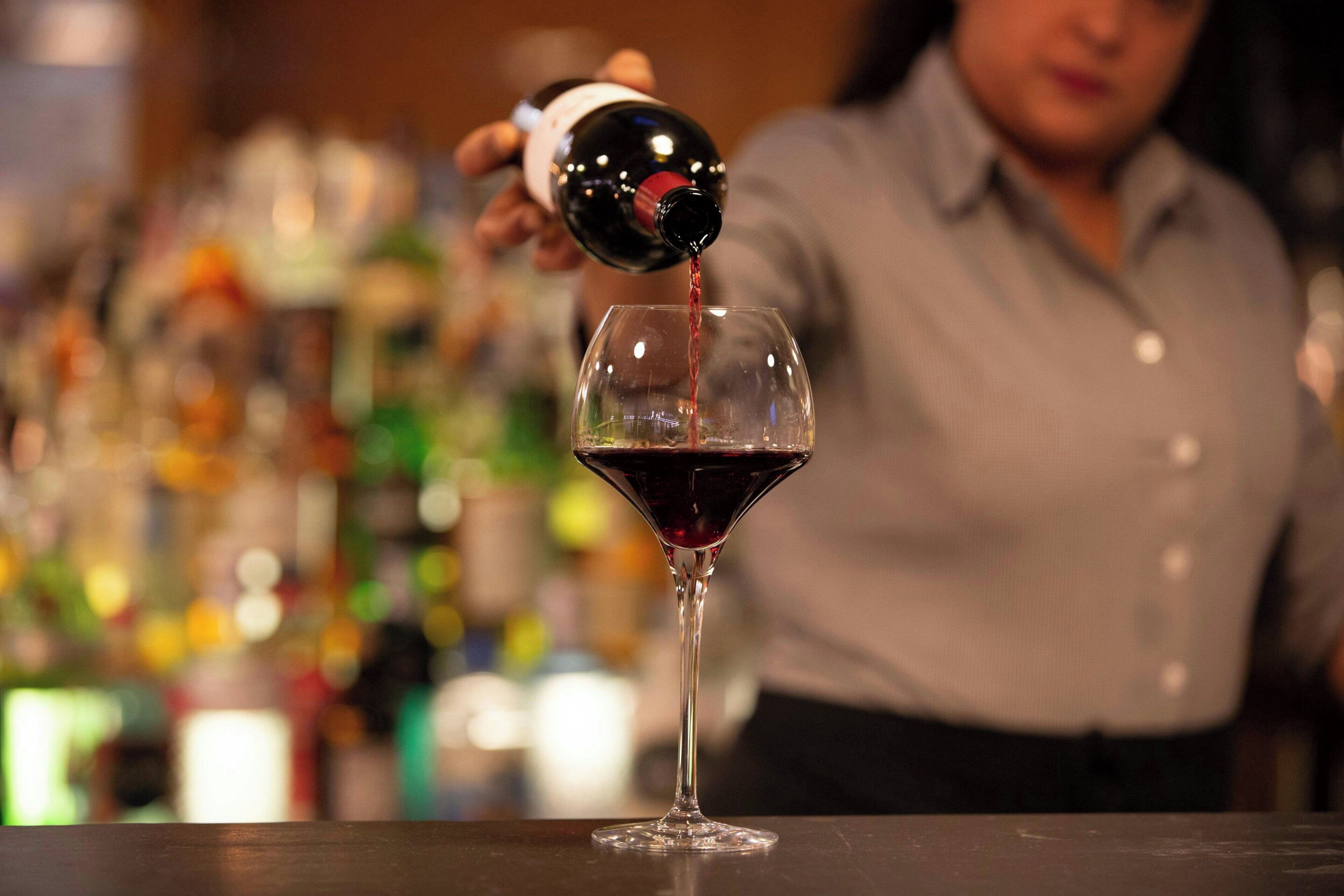 Une personne versant du vin rouge dans un verre à martini.