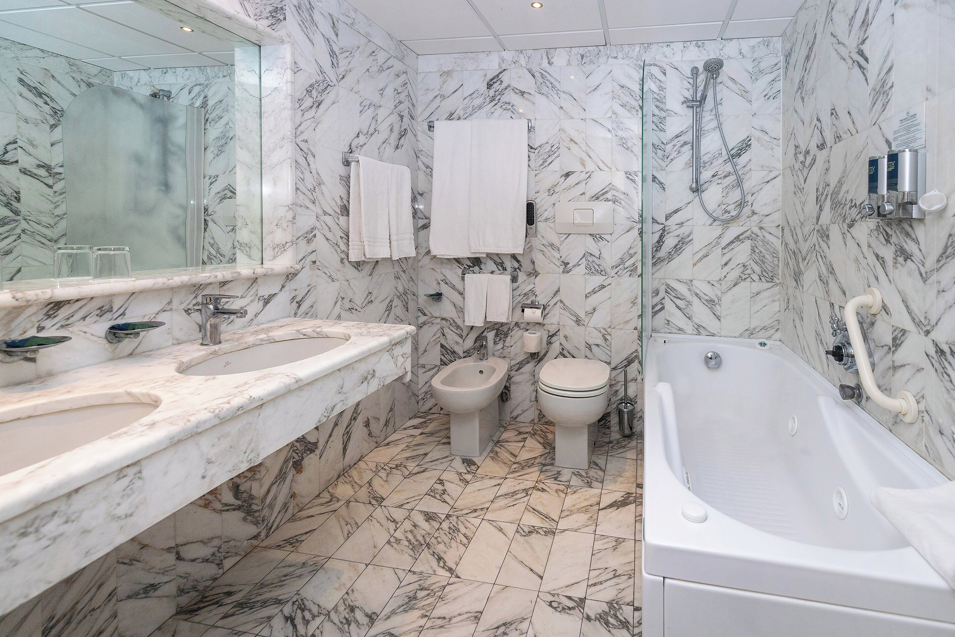 Un baño con pisos de mármol, una bañera grande, un bidé, un inodoro y un tocador con espejo y dos lavamanos.