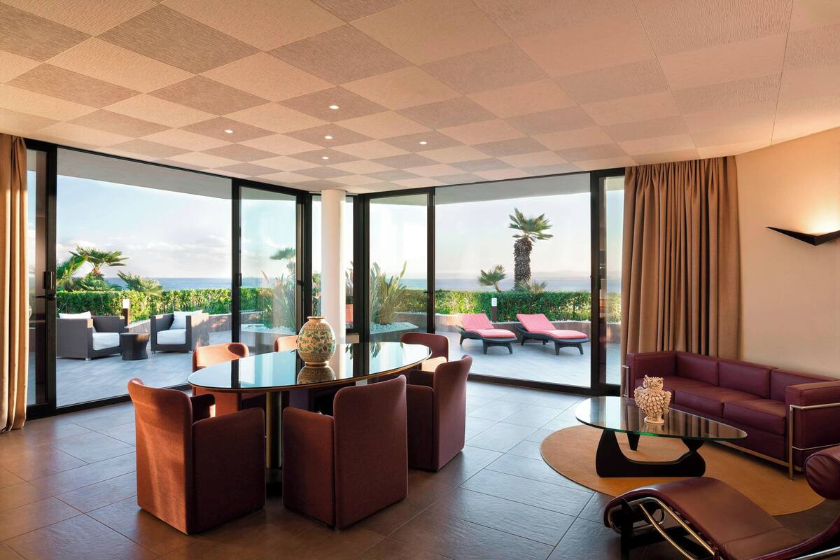Een moderne woonkamer met een glazen tafel en stoelen, een bank en uitzicht op de omgeving.